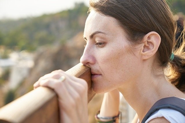 A woman feeling sad about her appearance due to dull skin and puffy eyes